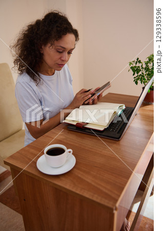 Woman Working from Home Using a Laptop, Phone, and Planner 129338596