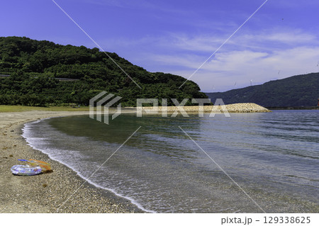 砂浜から望むムーンビーチ井野浦と防波堤、遠くに見える風車の夏景色 砂浜から望むムーンビーチ井野浦と防波堤、遠くに見える風車の夏景色 129338625