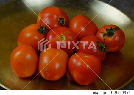 A pile of fresh, ripe tomatoes on a golden brass plate. 129339956