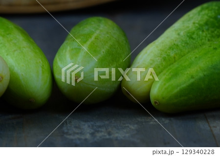 A horizontal line of fresh, green cucumbers laid out on a rustic wooden surface. 129340228