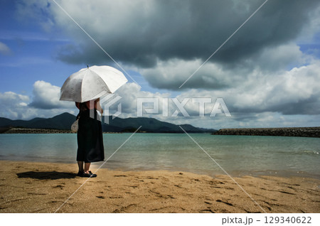 <素材>夏の海水浴場を散歩する日傘の女性 <素材>夏の海水浴場を散歩する日傘の女性 129340622
