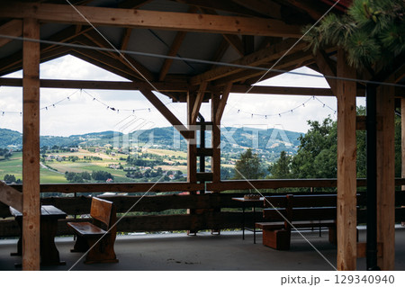 Wooden terrace overlooking scenic countryside hills with benches and string lights under a gabled roof. Rural tourism, destination marketing, peaceful retreats, eco-conscious travel 129340940