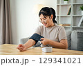 An Asian woman uses a portable blood pressure monitor in her living room. Health awareness concept. 129341021