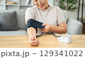 An Asian woman uses a portable blood pressure monitor in her living room. Health awareness concept. 129341022