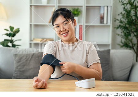 An Asian woman uses a portable blood pressure monitor in her living room. Health awareness concept. 129341023
