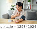 An Asian woman uses a portable blood pressure monitor in her living room. Health awareness concept. 129341024