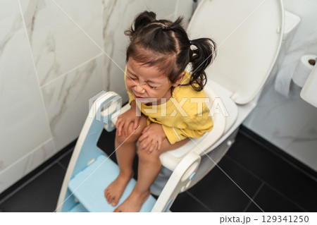 toddler girl sitting on toilet at home and suffering from stomachache and constipation toddler girl sitting on toilet at home and suffering from stomachache and constipation 129341250