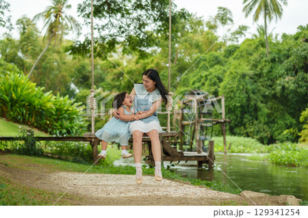 happy mother and toddler girl ride on wood swing in nature near the stream 129341254