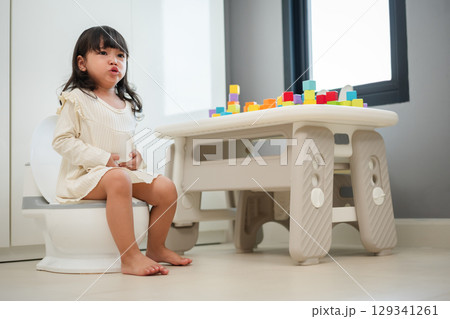 toddler gir learning sit on toilet wc seat at home. child being potty trained and suffering from stomachache and constipation 129341261