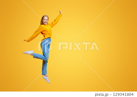 Be yourself. Pretty young girl jumping in air and laughing on orange background, free space 129341804