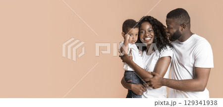 Family love. Portrait of young african american man and woman with their son on hands, yellow studio background with free space 129341938