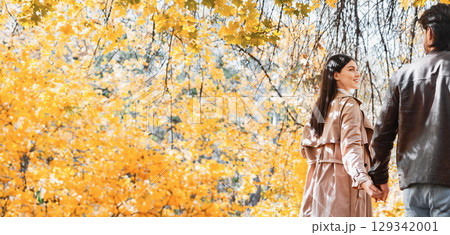 Man and woman holding hands and discovering golden autumn forest, back view 129342001