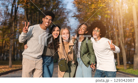 Cheerful multiethnic teenagers guys and girls posing at camera outdoors, showing peace gesture, park background Cheerful multiethnic teenagers guys and girls posing at camera outdoors, showing peace gesture, park background 129342007