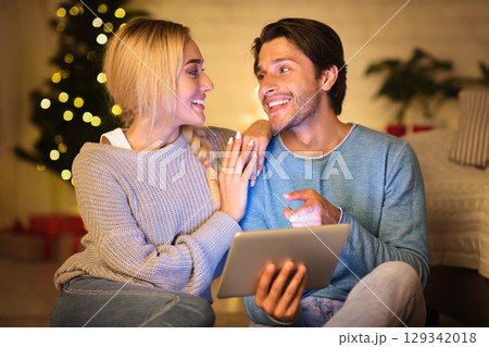 Joyful couple choosing film on tablet on Christmas eve, resting together at home 129342018