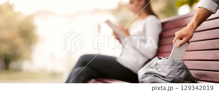Pickpocket Thief Stealing Mobile Phone From Woman's Bag While She Sitting On Bench In Park. Cropped, Selective Focus 129342019