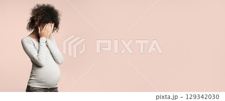 Depression during pregnancy. Afro woman covering face with hands and crying, grey background Depression during pregnancy. Afro woman covering face with hands and crying, grey background 129342030