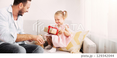 Birthday Girl. Excited daughter holding her present, happy father sitting nearby on the couch 129342044