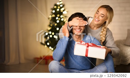 Cheerful woman having Christmas surprise for husband, closing his eyes from back Cheerful woman having Christmas surprise for husband, closing his eyes from back 129342092