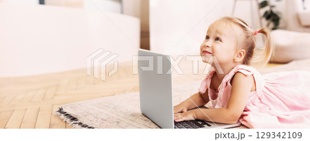 Modern Generation. Happy blonde toddler girl enjoying technologies playing indoors using laptop pc, copy space Modern Generation. Happy blonde toddler girl enjoying technologies playing indoors using laptop pc, copy space 129342109
