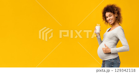 Pregnancy and calcium. Afro woman with glass of milk showing thumb up over pink studio background 129342118
