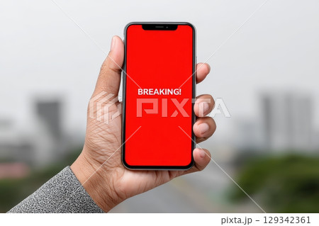 News alert displays breaking information on smartphone held by a person outdoors 129342361