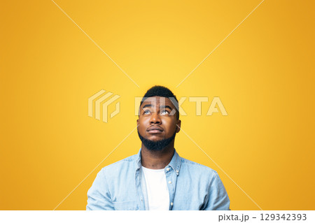 Doubtful african american man looking upwards at copy space on yellow background 129342393