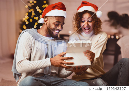 Christmas eve. Surprised spouses opening present box, enjoying evening at home Christmas eve. Surprised spouses opening present box, enjoying evening at home 129342397