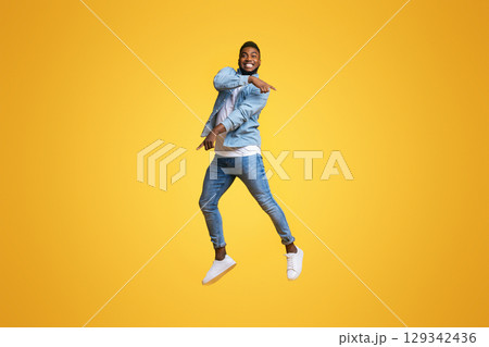 Look there. Funny african american man jumping in air and pointing at copy space over yellow studio background. 129342436