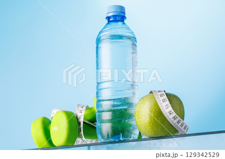 Bottle of water, green apple, and dumbbells on a glass table Bottle of water, green apple, and dumbbells on a glass table 129342529