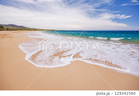 Sunny beach in Hawaii with golden sand, clear blue water under a bright sky 129342560
