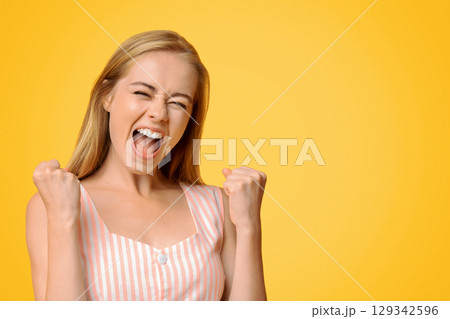 Crazy Sales. Pretty Young Girl Emotionally Shouting With Raised Fists, Celebrating Success Over Yellow Background, Copy Space 129342596