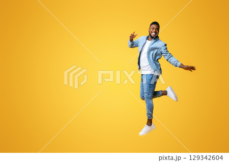 Portrait of funny black man jumping on yellow background with euphoric face expression, free space for text 129342604