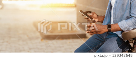 Modern Outdoor Leisure. Unrecognizable african man leaning on bicycle, using smartphone and drinking takeaway coffee outside 129342649