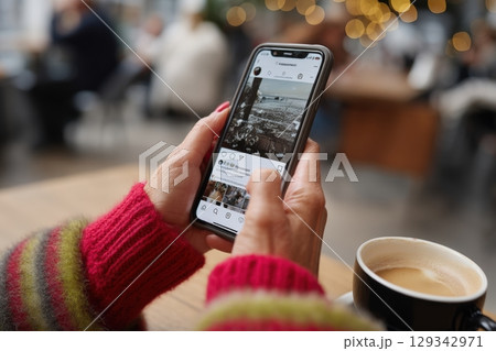 Enjoying a warm drink while scrolling through social media posts in a cozy cafe setting 129342971