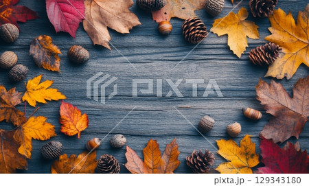 A vibrant arrangement of colorful autumn leaves, acorns, and pine cones forms a striking border on a dark wooden background. A vibrant arrangement of colorful autumn leaves, acorns, and pine cones forms a striking border on a dark wooden background. 129343180