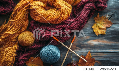 A vibrant display of yarn balls, knitting needles, and autumn leaves arranged on a rustic wooden surface, inviting creativity and warmth. A vibrant display of yarn balls, knitting needles, and autumn leaves arranged on a rustic wooden surface, inviting creativity and warmth. 129343224