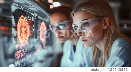 Two researchers focus intently on digital brain scans in a modern laboratory, wearing protective eyewear and lab coats. 129343321