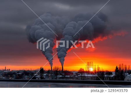 Smoke billows from industrial chimneys at sunset over a frozen river landscape 129343570