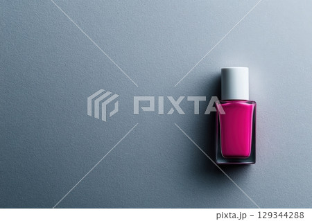 Bright pink nail polish bottle on a smooth grey surface showcasing vibrant color 129344288
