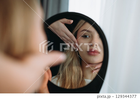 young woman looking in a mirror after facian rejuvenation procedure at aesthetic clinic young woman looking in a mirror after facian rejuvenation procedure at aesthetic clinic 129344377