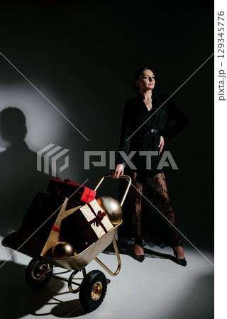 Woman Posing with Gift-Filled Wheelbarrow in Stylish Attire Woman Posing with Gift-Filled Wheelbarrow in Stylish Attire 129345776