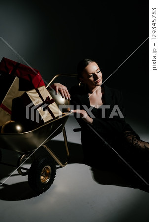 Pensive Woman by Gift Cart with Presents in Dark Setting 129345783