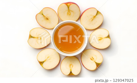 Sliced apples arranged around a bowl of apple cider on a white background 129347025