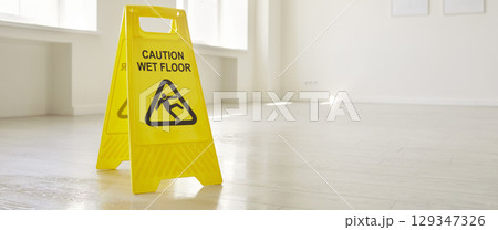 Close up of caution wet floor sign standing on floor in empty room or office with copy space. Close up of caution wet floor sign standing on floor in empty room or office with copy space. 129347326