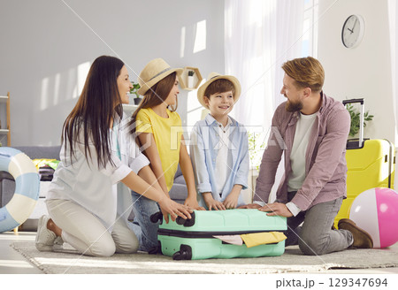 Happy moment when parents and children close packed suitcase together before summer trip. 129347694