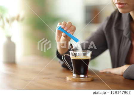 Woman hand throwing sugar in a coffee cup on a table at home 129347967