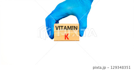 Vitamin K phylloquinone symbol. Concept words Vitamin K on beautiful wooden blocks. Doctor's hand medical glove. Beautiful white background. Medical healthy lifestyle Vitamin K phylloquinone concept. 129348351