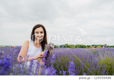 A girl with long dark hair has sat down in the middle of a lavender field A girl with long dark hair has sat down in the middle of a lavender field 129350490