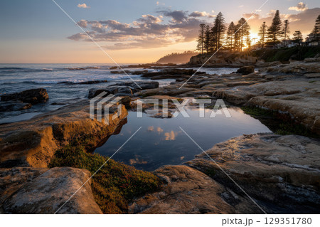Colorful sunset reflected in tidal pools on rocky shore 129351780