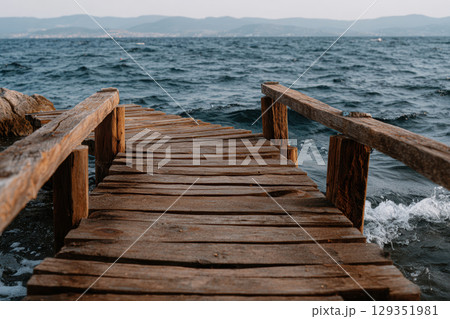 Rustic wooden pier leading into calm ocean waters at dusk 129351981